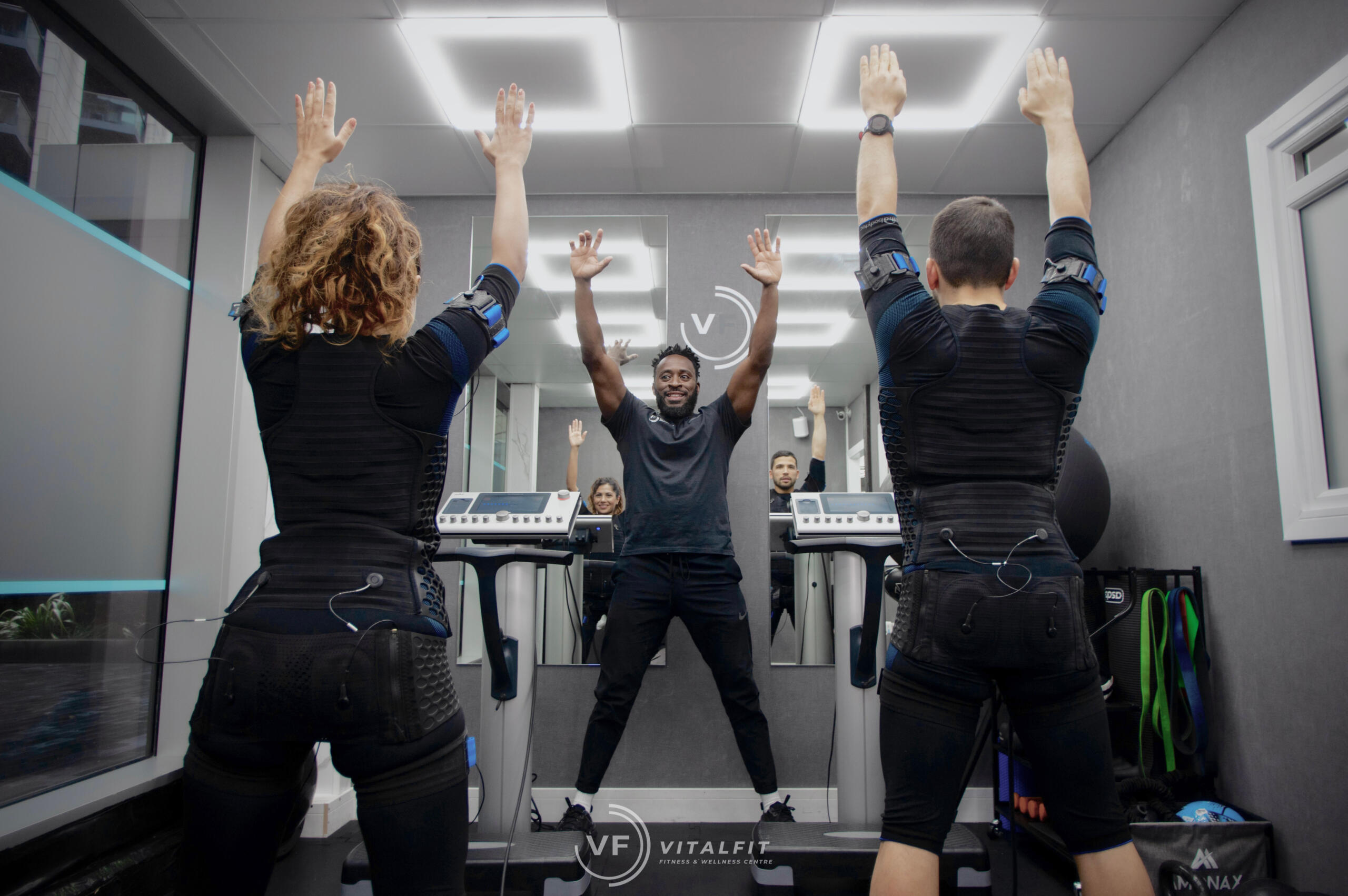 Two people participating in an EMS training session, wearing EMS suits, guided by an instructor in Vitalfit.